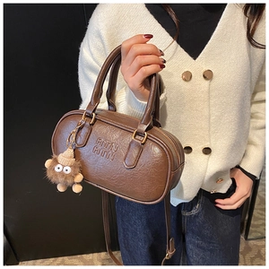 Détail du sac Boston marron caramel avec texture cuir et pendentif monstre en peluche
