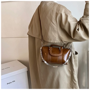 Brown vintage leather handbag with metal chain shown on a model in a trench coat