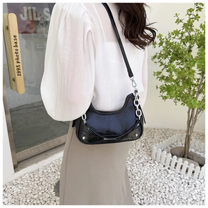 Détail d'un sac plissé noir brillant avec chaîne argentée et rivets dans un décor extérieur