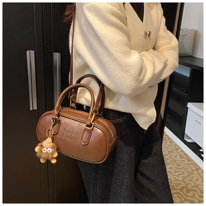 Détail d'un sac tonneau en cuir marron avec logo ATN et breloque en peluche monstre
