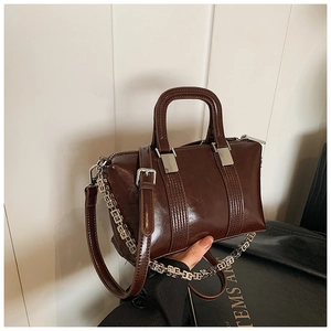 Detail of glossy dark brown leather boston bag featuring a silver designer metal chain