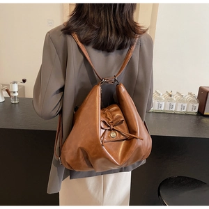 Close-up of caramel brown leather backpack with bow detail and vintage metal button
