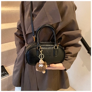 Détail du sac Boston noir en cuir grainé avec boucle dorée et breloque en peluche marron