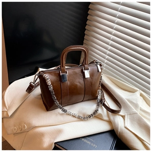Detail of dark brown retro Boston bag with silver chain on beige blazer background