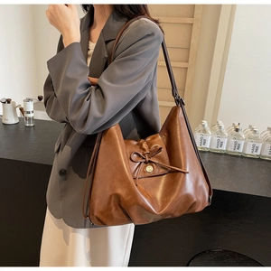 Detail view showing brown leather tote bag with bow knot decoration and golden buckle
