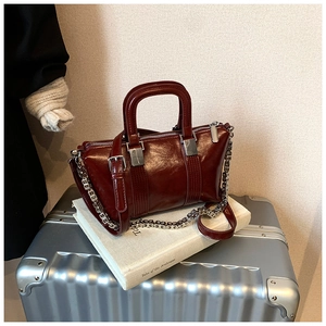 Detail of vintage burgundy leather handbag with silver chain on a suitcase for travel
