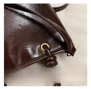 Dettaglio della texture in pelle marrone scuro e finiture dorate su borsa a secchiello