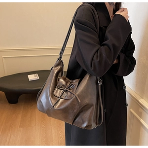 Detail of dark brown leather tote featuring a retro bow drawstring and metal buckle closure