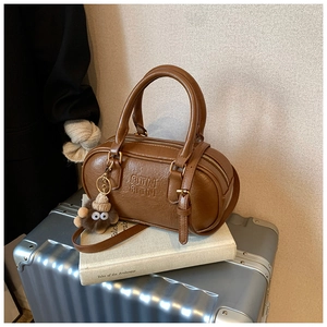 Détail du sac Boston marron avec texture litchi et breloque en peluche monstre mignonne