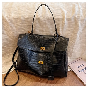 Detail of black crocodile texture tote bag with brass metal clasp and adjustable strap