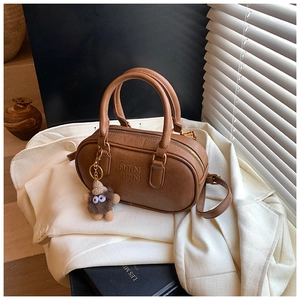 Gros plan détaillé d'un sac Boston en cuir marron avec logo embossé et breloque peluche