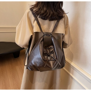 Detail of vintage brown leather backpack with bow and button on beige trench coat