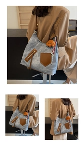 Dettaglio borsa tote in denim blu con tasca in pelle marrone e ciondolo a forma di orso