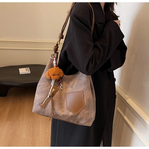 Vista dettagliata della borsa tote marrone retrò con ciondolo a forma di orso e texture opaca