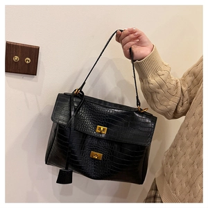 Detail of black crocodile pattern tote bag with golden twist-lock buckles held by model