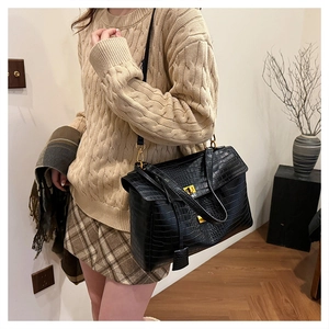 Detail of black crocodile texture tote bag with gold metal buckle lock and long strap