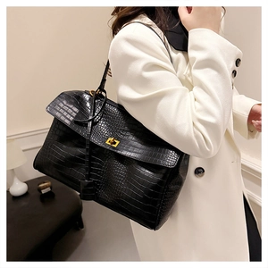 Detail of black crocodile texture leather tote with golden twist lock on white coat