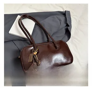 Détail d'un sac Boston en cuir marron foncé brillant avec breloques vintage et zip doré