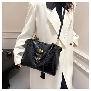 Close-up of black crocodile pattern tote bag with gold twist lock on white suit