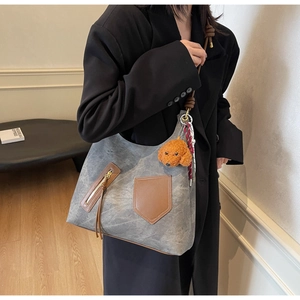 Dettaglio della borsa tote in tessuto grigio con finiture in pelle marrone e ciondolo a orso