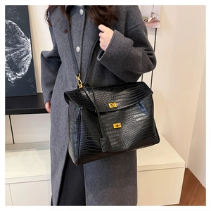 Detail of black crocodile pattern leather tote bag with gold hardware on a gray coat