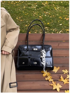 Detail of black glossy leather satchel with silver twist lock and chic pendant on wood bench