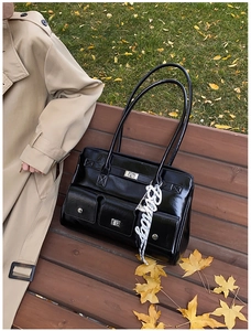 Detail of black glossy leather briefcase with silver twist locks and decorative white charm