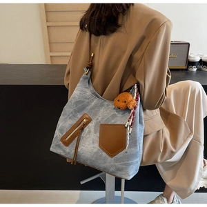 Dettaglio della borsa tote in denim blu con tasche in pelle marrone e ciondolo