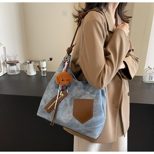 Dettaglio della borsa tote in denim blu lavato con tracolla in pelle e ciondolo a peluche