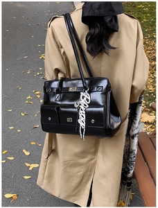 Detail of black glossy leather messenger bag with silver clasp and letter charm