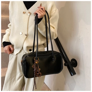 Gros plan d'un sac Boston noir brillant avec breloque clé dorée et détails tressés