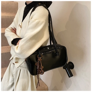 Détail du sac Boston noir brillant avec breloque tressée et pendentif clé dorée