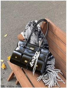 Detail of a black glossy briefcase bag with gold twist locks and a white bag charm