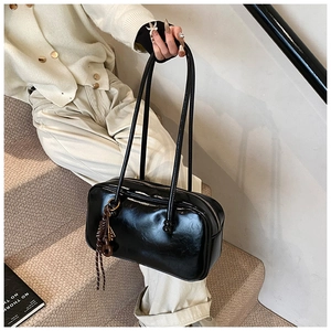 Détail du sac Boston en similicuir noir brillant avec un charmant pendentif tressé