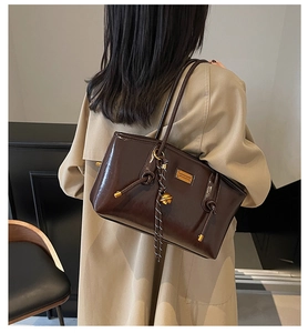 Detail of dark brown glossy leather tote bag featuring gold bell and striped cord