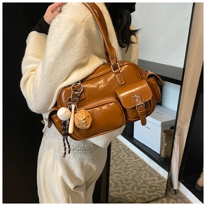 Brown leather bowling bag with side pockets and baseball charm shown on shoulder