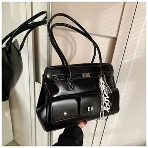 Close-up of black glossy leather satchel bag featuring two front pockets with metallic buckles