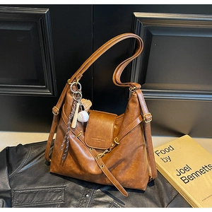 Detail of caramel brown leather tote bag featuring a baseball charm and embossed fashion text