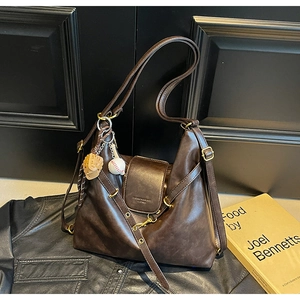 Detail of dark brown vintage faux leather shoulder bag with a unique baseball charm on black leather