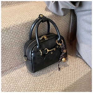 Close-up of black leather Boston bag with golden horsebit detail and woven charm