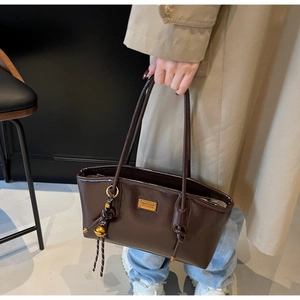 Detail of glossy oil wax leather tote bag featuring a gold logo plate and metal charm