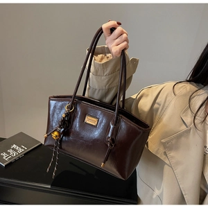 Detail view of coffee brown oil wax leather shoulder bag with gold metal plate and bell charm