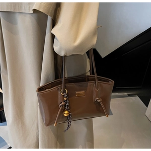 Close-up of deep brown glossy oil wax leather tote bag with gold logo and bead charm
