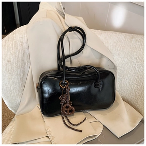 Vue détaillée d'un sac Boston en cuir noir brillant avec un pendentif nœud tressé