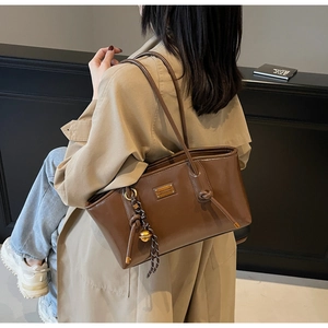 Detail of brown oil wax leather tote bag with metallic plaque and woven charm on handle