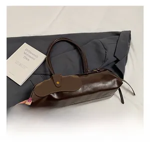 Detail view of a retro dark brown oil wax leather baguette bag with gold button closure