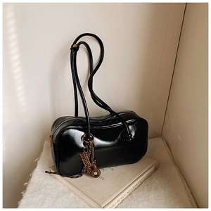 Détail du sac Boston en cuir brillant noir avec chaîne décorative sur tissu blanc
