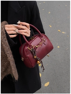 Detail of burgundy leather Boston bag with vintage hardware and woven pendant on autumn ground