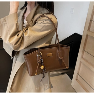 Close-up of dark brown faux leather tote bag with metal logo and knotted tassel detail