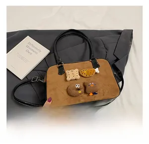 Detail of a brown suede bowling bag with cute cartoon food badges and black leather handles